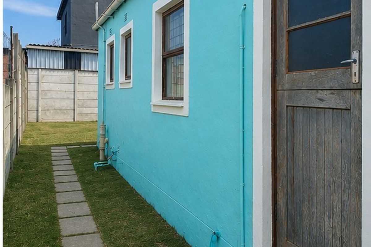 A side view of the property featuring a bright blue exterior wall, a timber door, and a paved walkway leading along the lawn.