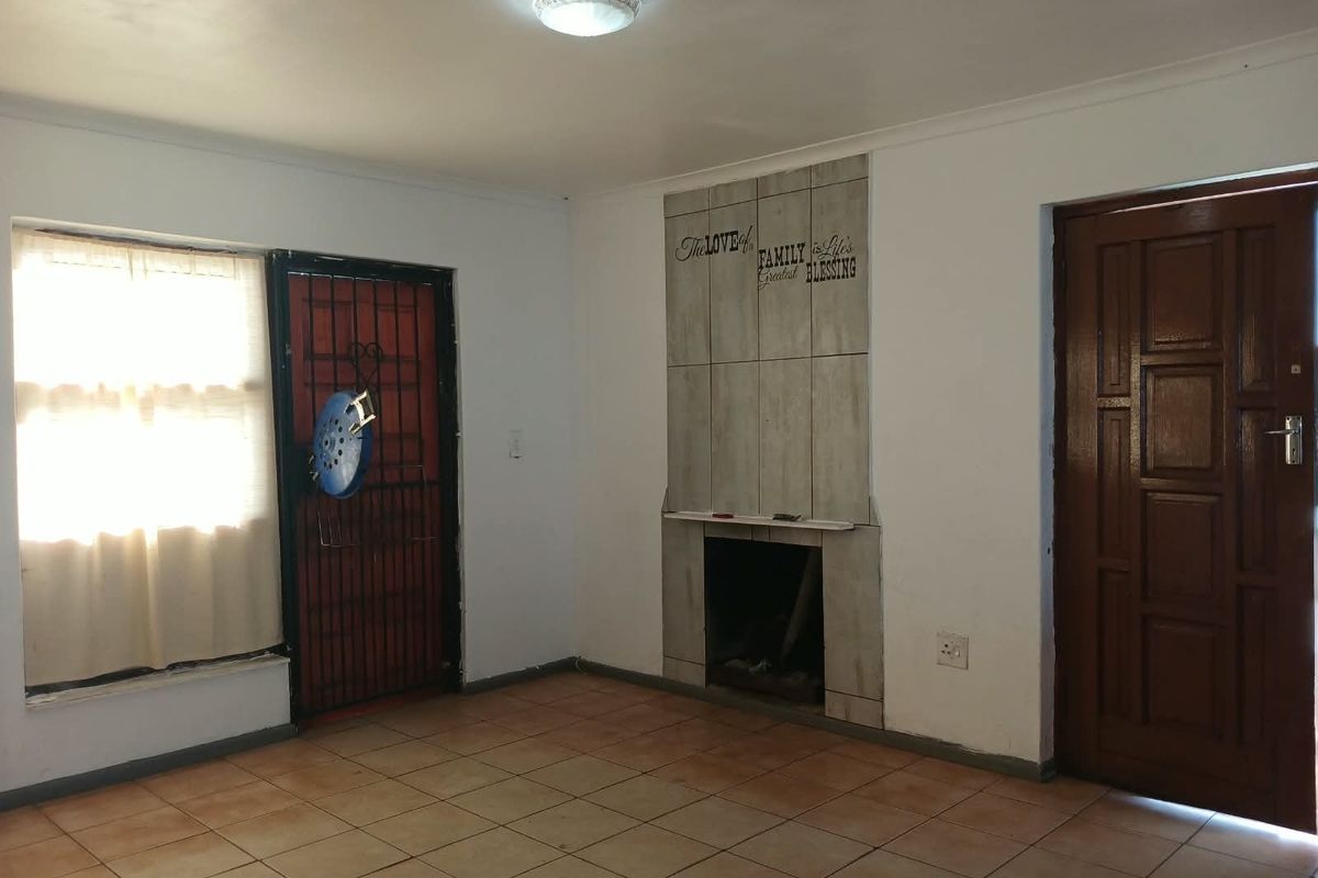 An empty living room featuring tiled flooring, a built-in fireplace with decorative tiling, and access to a security gate and wooden door.