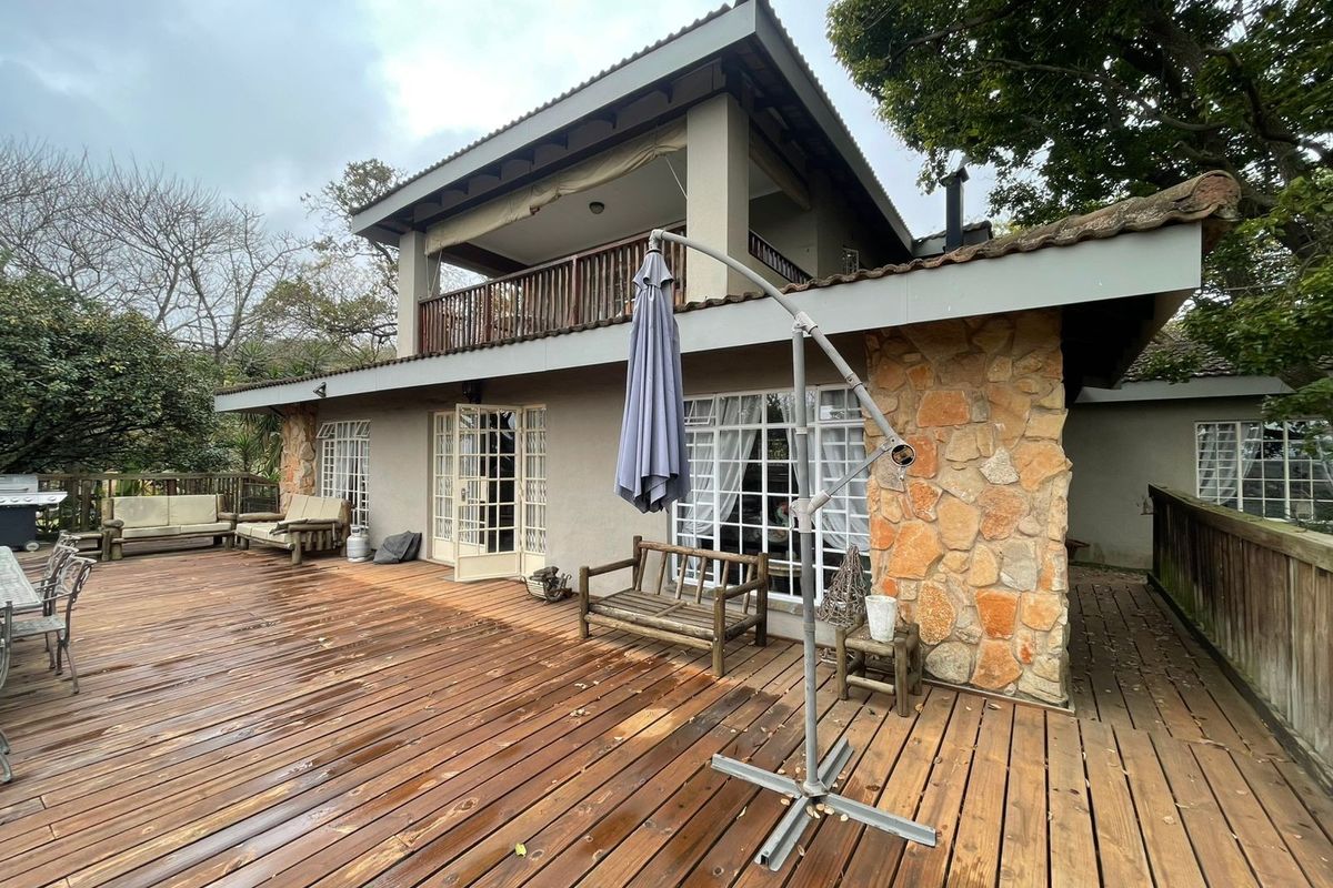 Spacious rear exterior featuring a large timber deck, stone-clad feature wall, and an upper-level balcony with timber balustrades.
