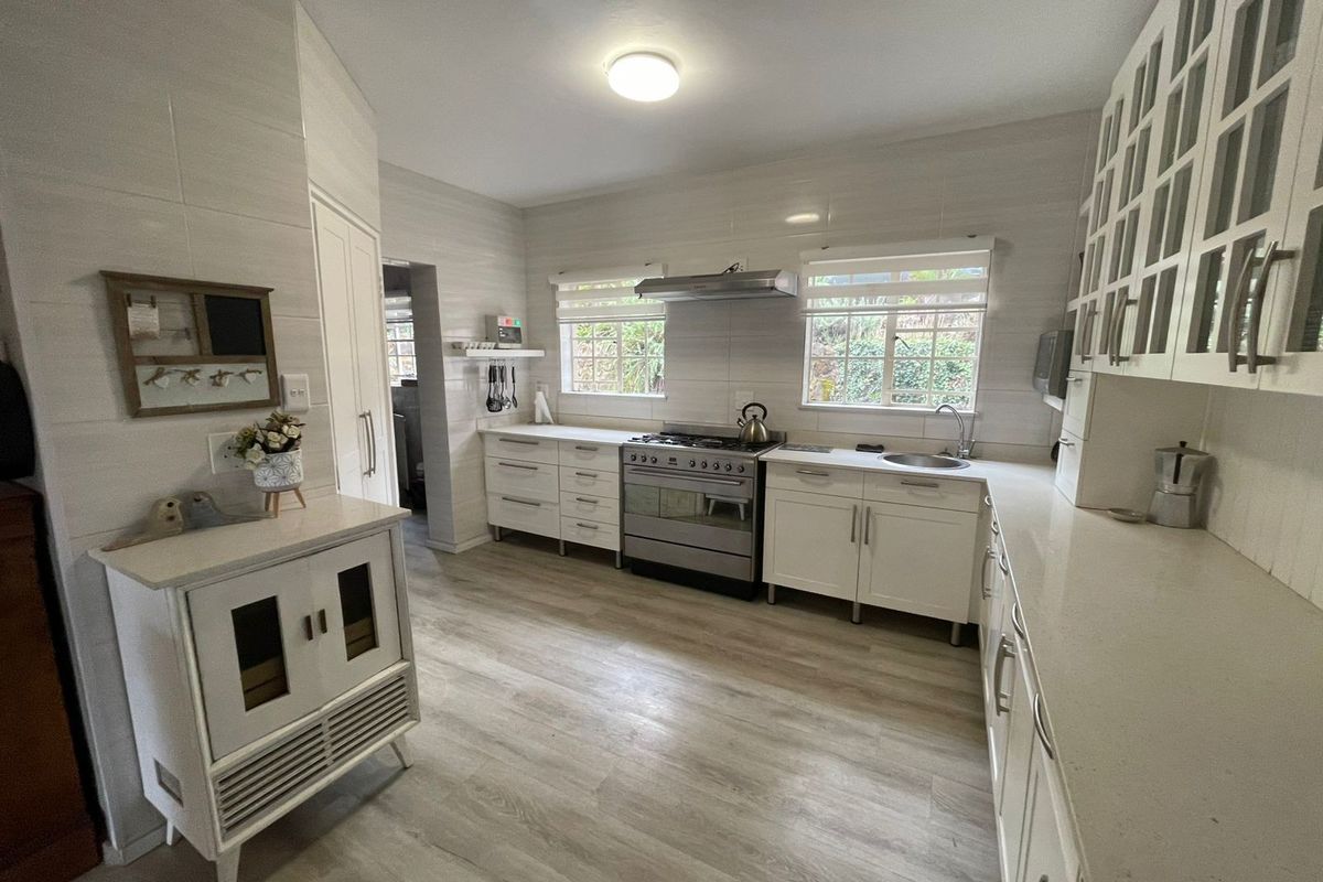 A bright, well-maintained kitchen featuring white cabinetry, stone countertops, a gas stove with extractor fan, and modern laminate flooring.