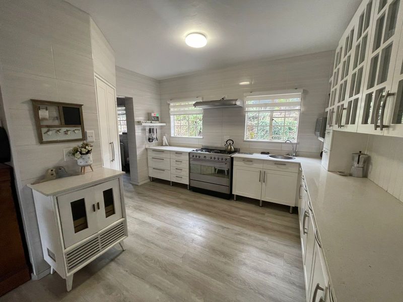 A bright, well-maintained kitchen featuring white cabinetry, stone countertops, a gas stove with extractor fan, and modern laminate flooring.