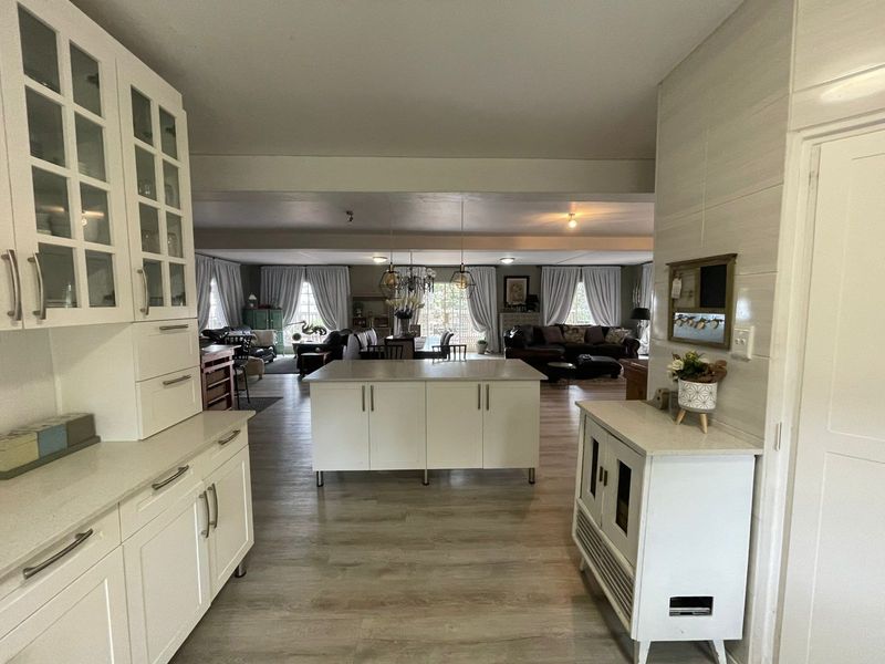 Spacious open-plan living area featuring a modern kitchen with white cabinetry, a central island, and light-toned laminate flooring flowing into the lounge.