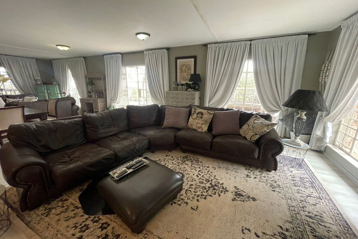 Spacious living room featuring laminate flooring, multiple windows with security gates, and flush mount lighting, offering a comfortable and functional family space.