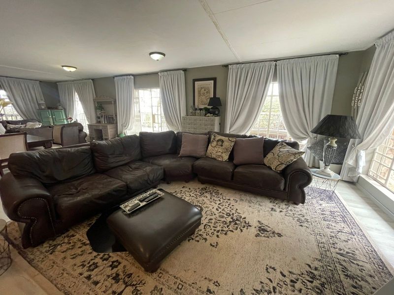 Spacious living room featuring laminate flooring, multiple windows with security gates, and flush mount lighting, offering a comfortable and functional family space.