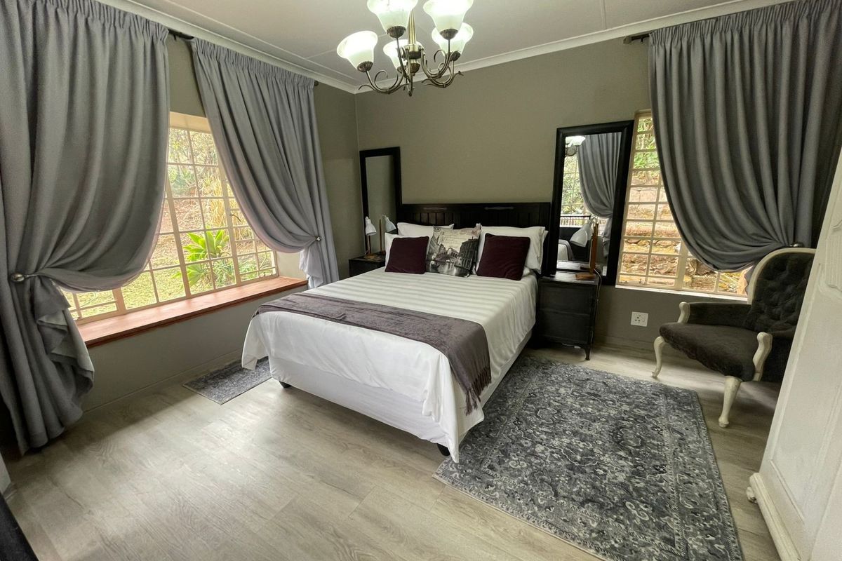 A well-maintained bedroom featuring laminate flooring, large windows with natural light, and a classic chandelier fixture.