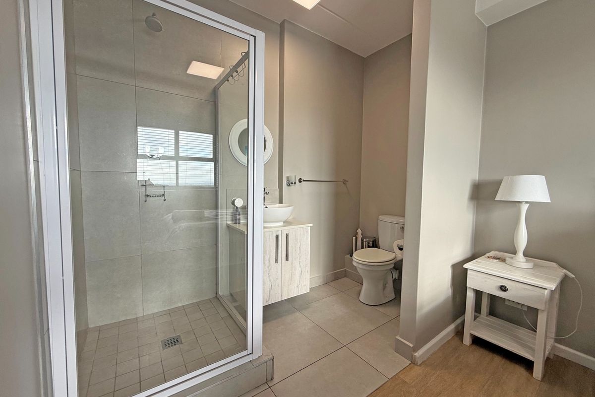 Modern bathroom featuring a glass-enclosed shower, vessel sink with vanity cabinet, and a standard toilet, finished with neutral floor and wall tiling.