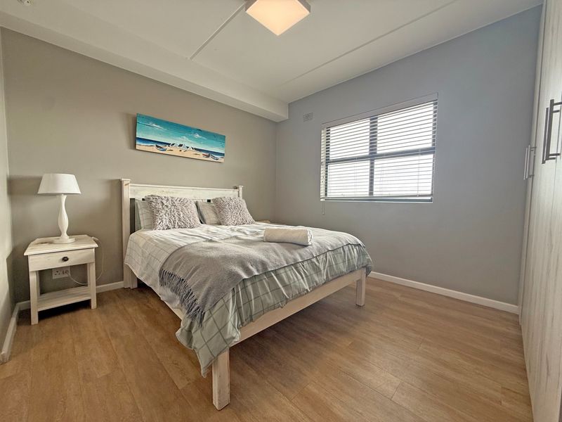 A well-maintained bedroom featuring light laminate flooring, neutral wall tones, a built-in wardrobe, and venetian blinds for adjustable natural light.