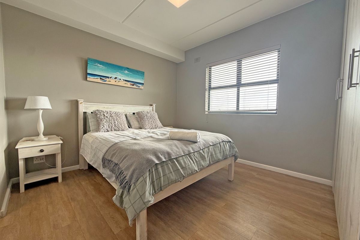 A well-maintained bedroom featuring light laminate flooring, neutral wall tones, a built-in wardrobe, and venetian blinds for adjustable natural light.