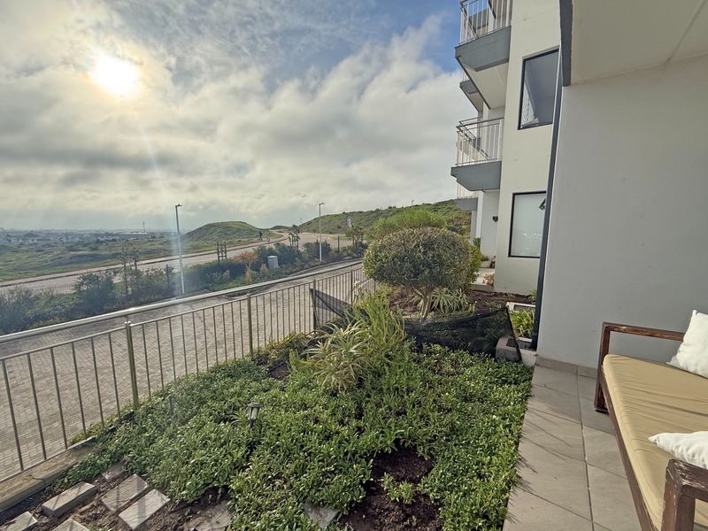 A ground-floor patio featuring tiled flooring, a metal balustrade, and a landscaped garden bed with views of the surrounding landscape.