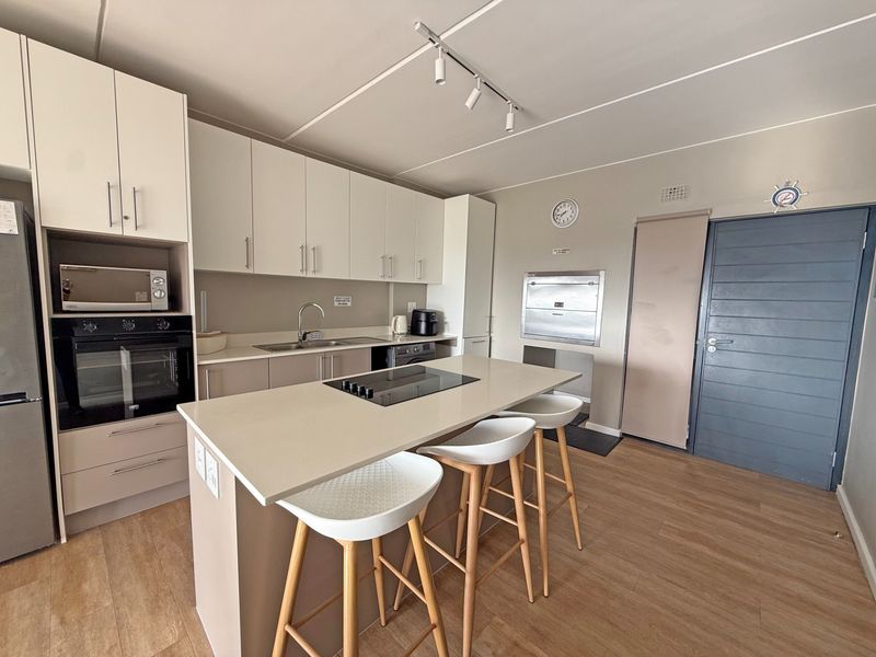 Modern kitchen featuring a central island with an integrated electric hob, ample built-in cabinetry, stone countertops, and high-quality built-in appliances.