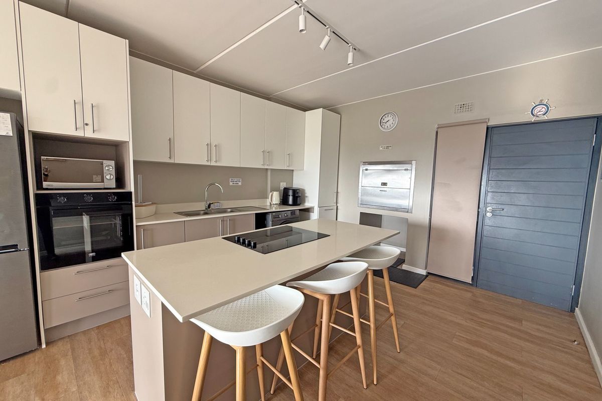 Modern kitchen featuring a central island with an integrated electric hob, ample built-in cabinetry, stone countertops, and high-quality built-in appliances.
