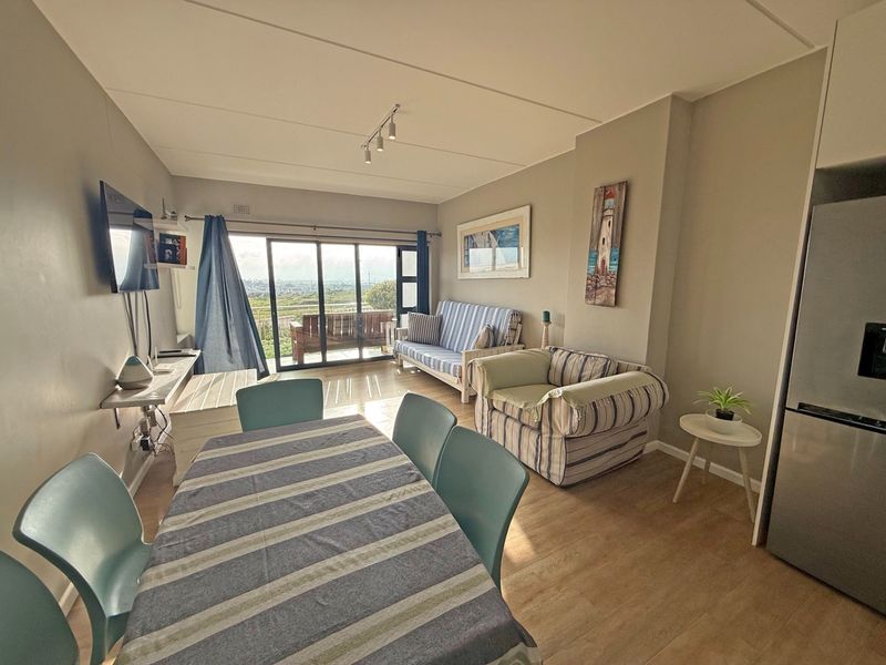 Open-plan living and dining area featuring laminate flooring, track lighting, and large sliding glass doors leading to an outdoor balcony with scenic views.