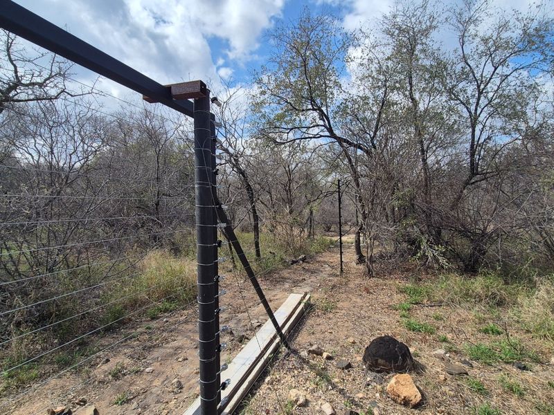 A view of the property boundary featuring an installed electric fence system set against a natural, wooded landscape.