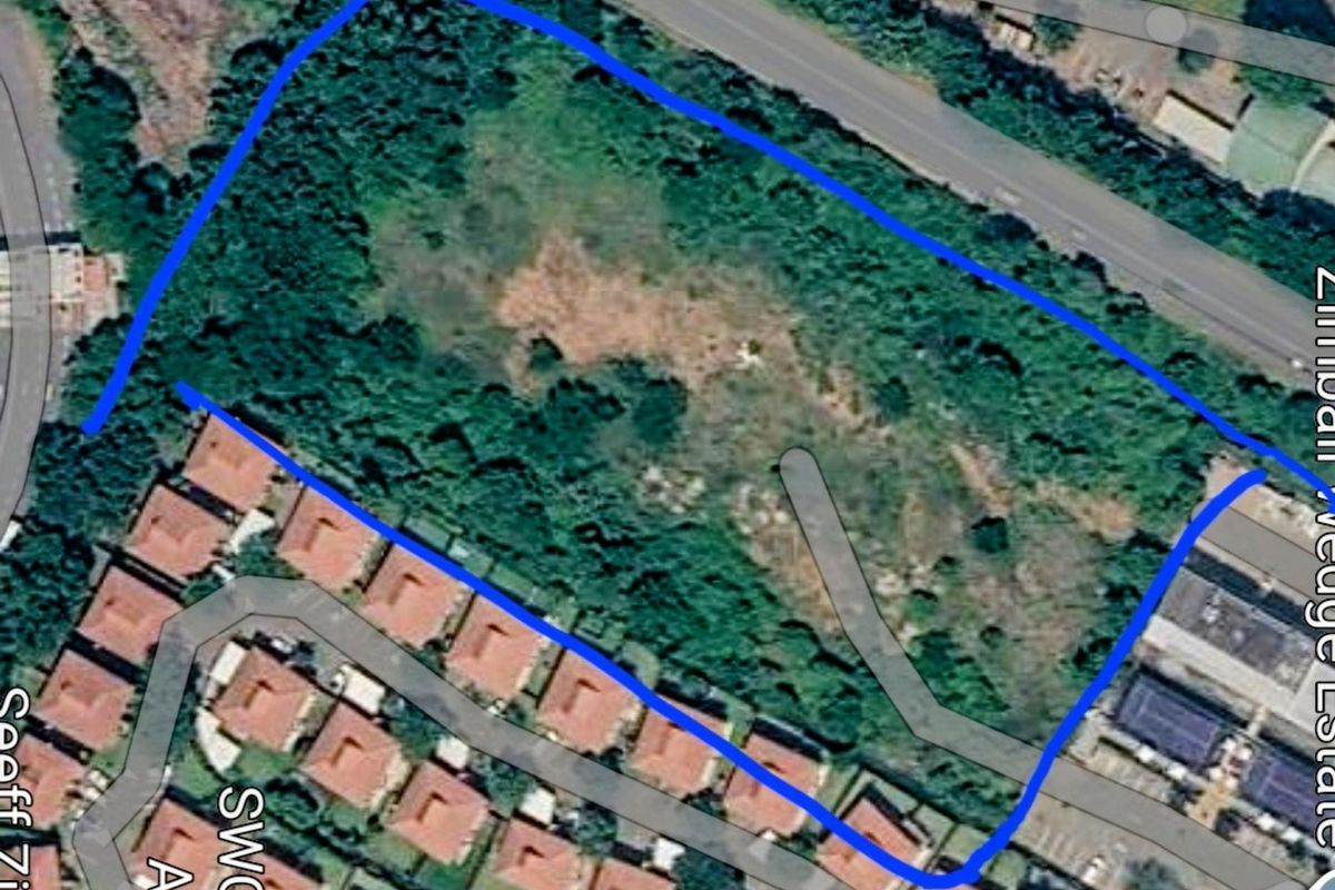 An aerial view of a vacant residential plot of land surrounded by established residential housing and road infrastructure.