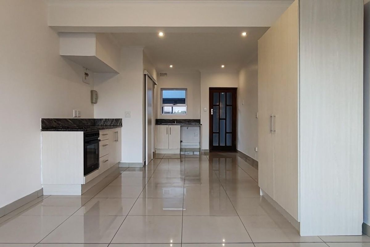 An open-plan living and kitchen area featuring neutral ceramic floor tiles, modern built-in cabinetry, granite countertops, and integrated storage cupboards.