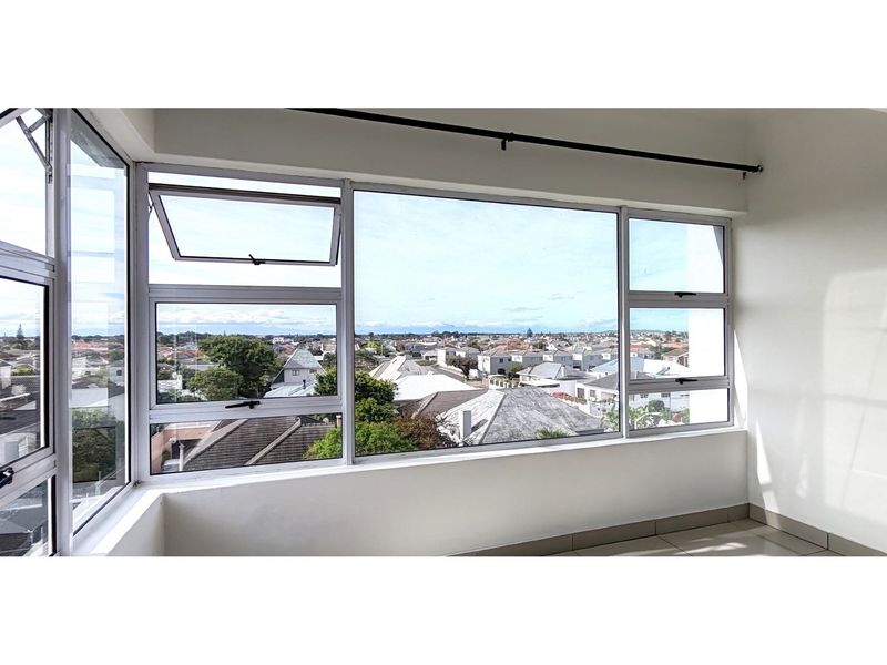 An enclosed balcony or sunroom featuring large aluminium-framed windows with expansive neighbourhood views and neutral tiled flooring.