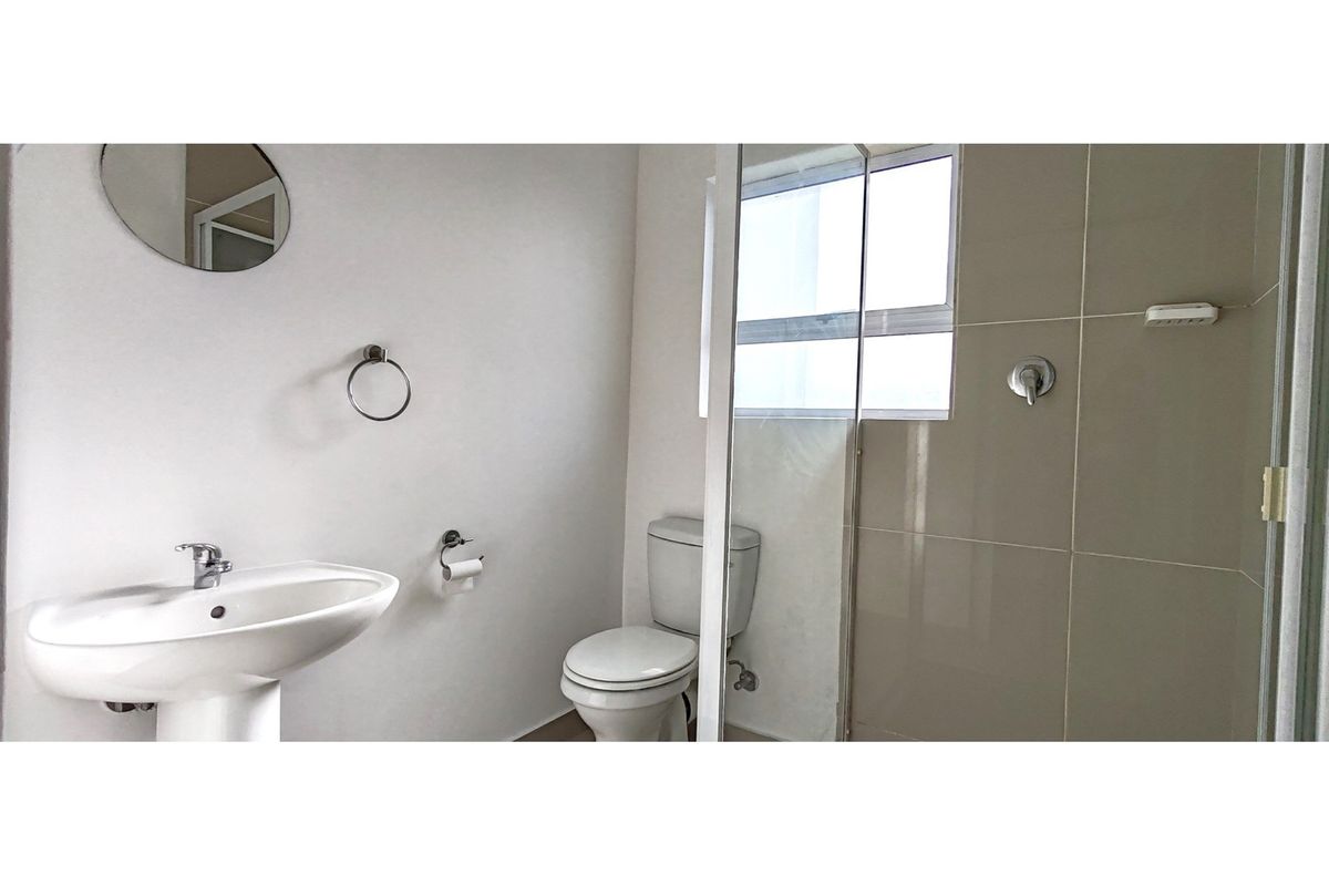 A clean, functional bathroom featuring a pedestal basin, toilet, and a glass-enclosed shower with neutral wall tiling.