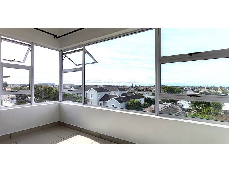 An enclosed balcony or sunroom featuring large aluminium-framed windows with expansive neighbourhood views and neutral tiled flooring.