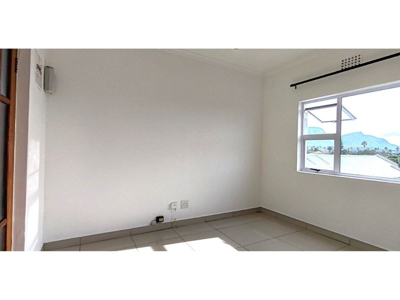 A bright, empty bedroom featuring neutral tiled flooring, clean white walls, and a large window with mountain views.