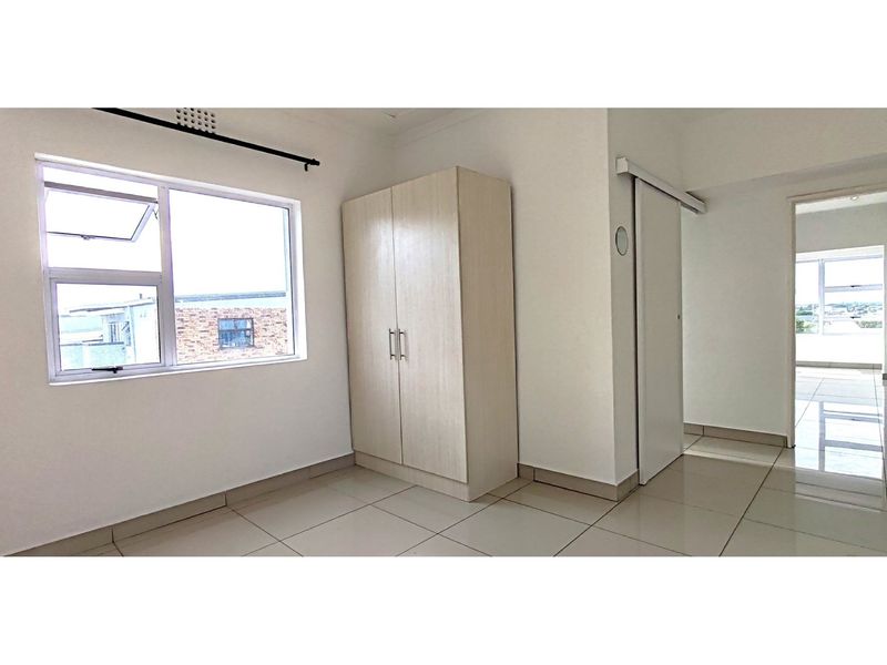 A bright, empty bedroom featuring neutral tiled flooring, a built-in wardrobe, and a sliding door leading to an adjacent living area.