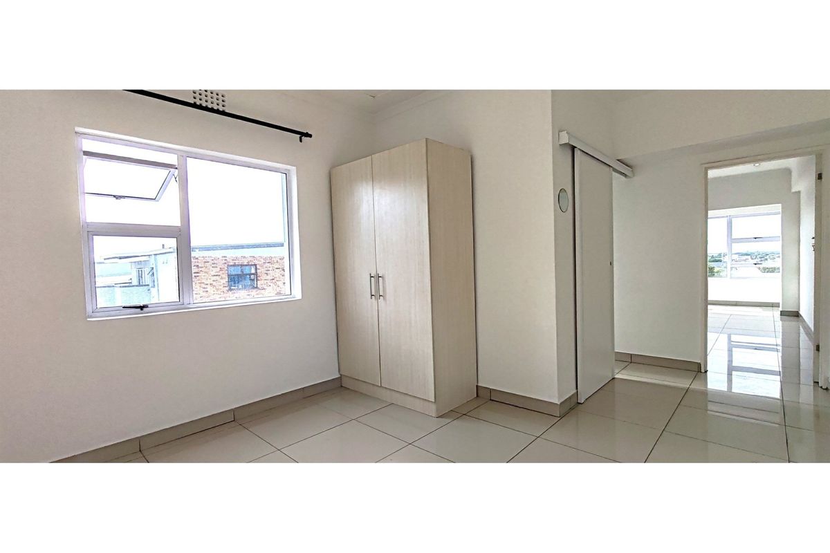 A bright, empty bedroom featuring neutral tiled flooring, a built-in wardrobe, and a sliding door leading to an adjacent living area.