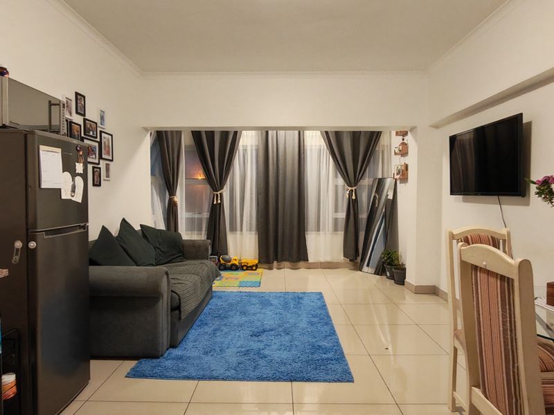 Open-plan living and dining area featuring neutral tiled flooring and a wall-mounted television, providing a versatile space for relaxation and meals.