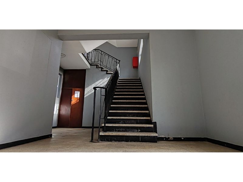 A communal apartment building hallway featuring a central staircase with metal handrails and tiled flooring.