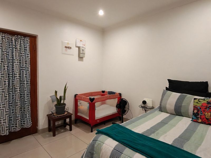 A bedroom featuring tiled flooring, recessed downlighting, and a wooden door, providing a functional and neutral living space.
