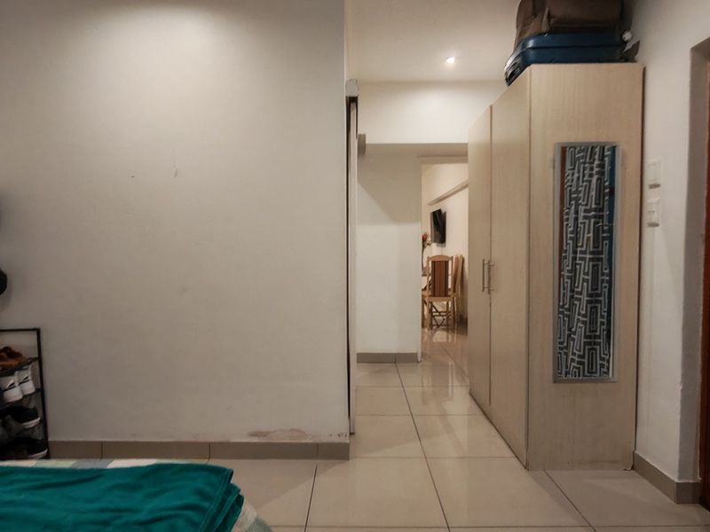 A bedroom featuring tiled flooring, a built-in wardrobe, and recessed lighting, with a view leading into an adjacent living area.