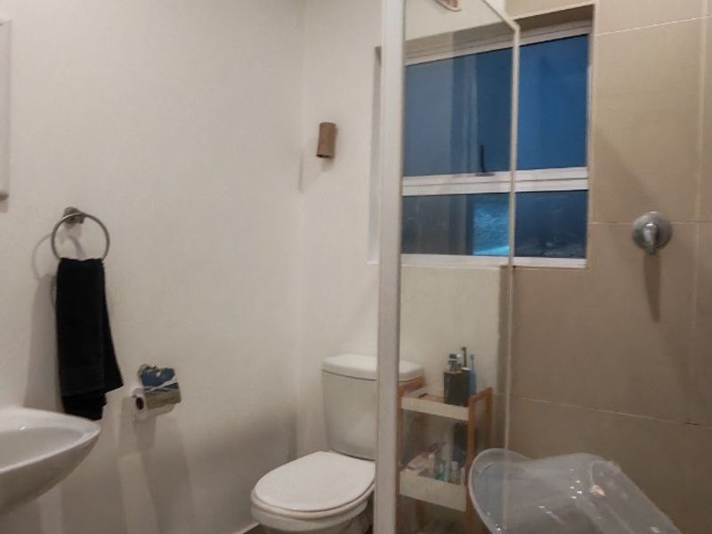 A functional bathroom featuring a shower enclosure, toilet, and washbasin with neutral wall and floor tiling.