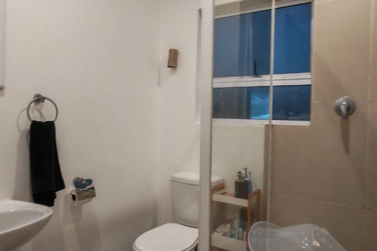A functional bathroom featuring a shower enclosure, toilet, and washbasin with neutral wall and floor tiling.