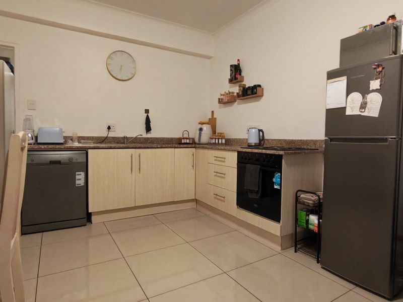 Functional kitchen featuring light wood-finish cabinetry, granite countertops, built-in oven, ceramic hob, and tiled flooring in an open-plan layout.