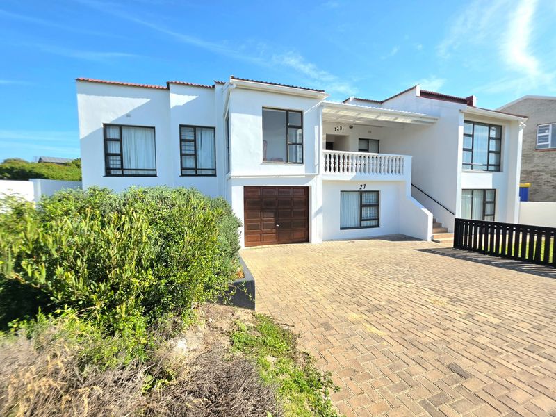 Front elevation of a multi-level residential property featuring a paved driveway, integrated garage, and an upper-level balcony with a classic balustrade.