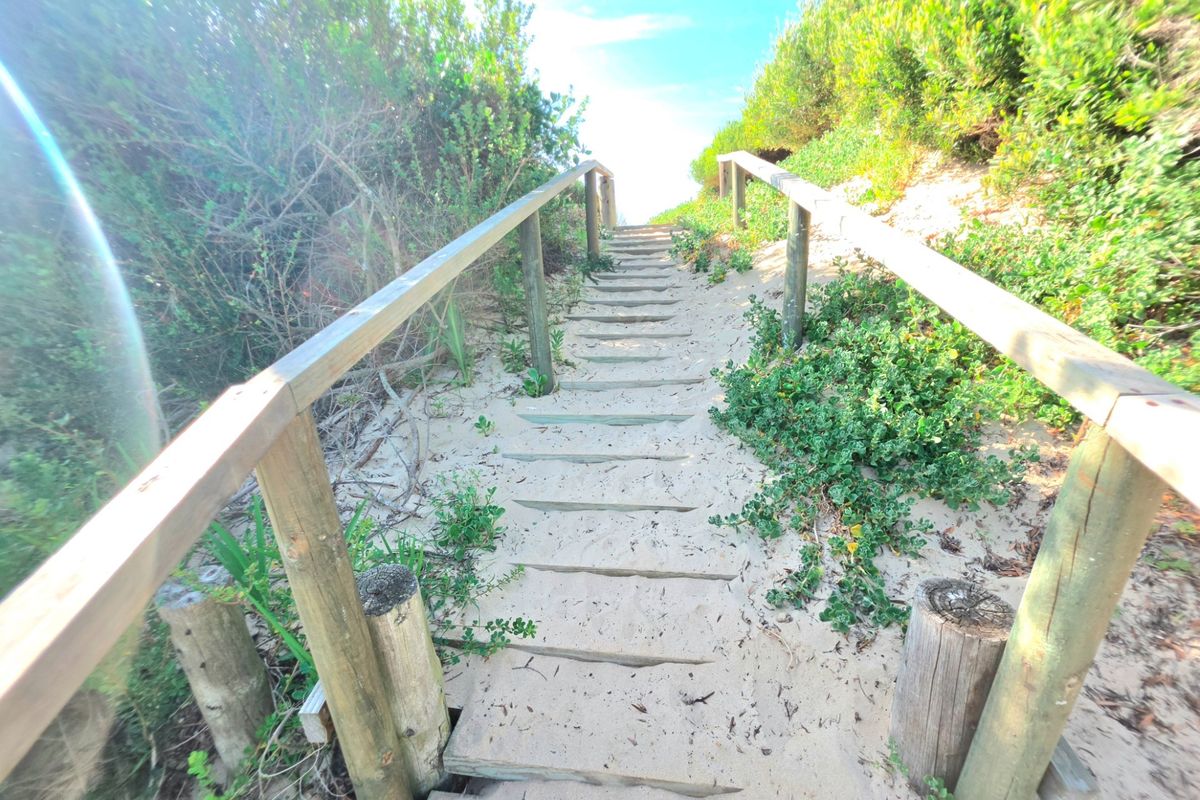 A timber staircase leading through a sandy path and coastal vegetation, providing direct outdoor access.