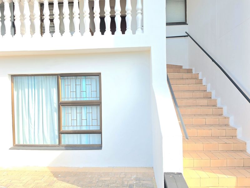 Exterior view of the property featuring a tiled staircase with a metal handrail, a balcony with a balustrade, and security-barred windows.