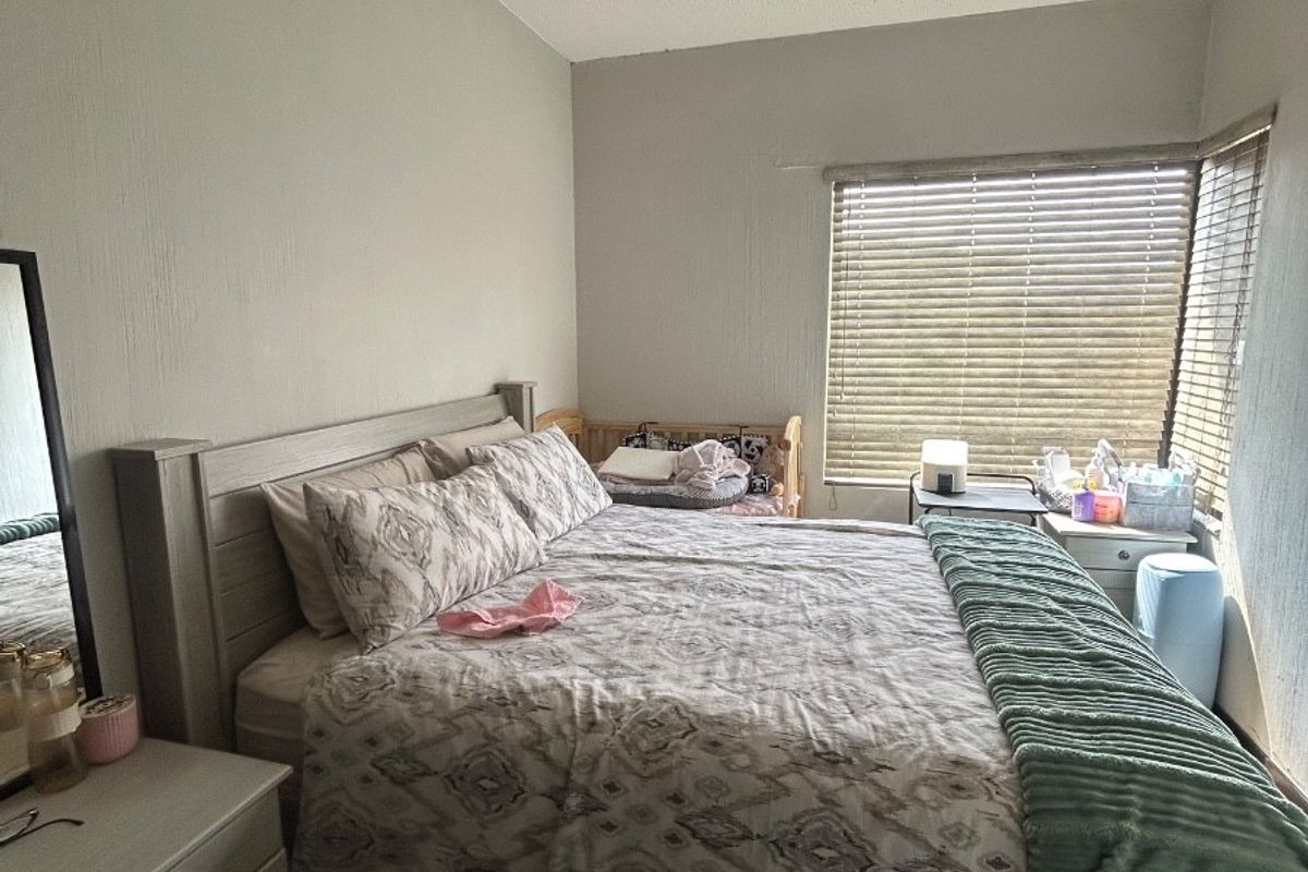 A functional bedroom featuring neutral wall finishes, corner window placement with venetian blinds, and a ceiling-mounted spotlight fixture.
