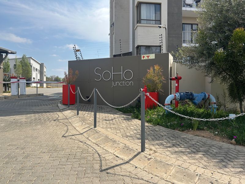 The entrance to SoHo Junction apartment complex featuring paved driveway, security boom gate, and perimeter electric fencing.