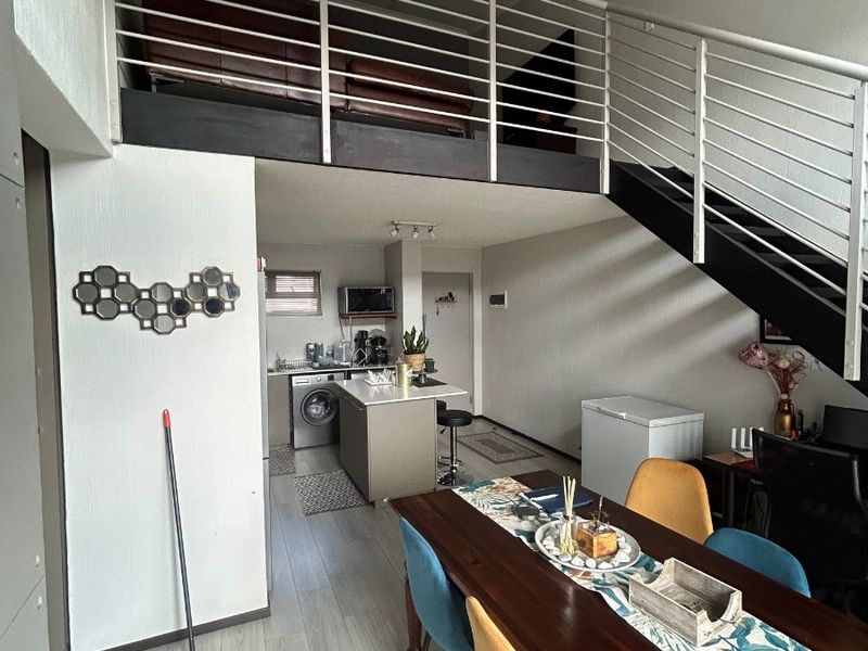 Open-plan living area featuring a mezzanine level with metal staircase, modern laminate flooring, and a functional kitchen with a central island.