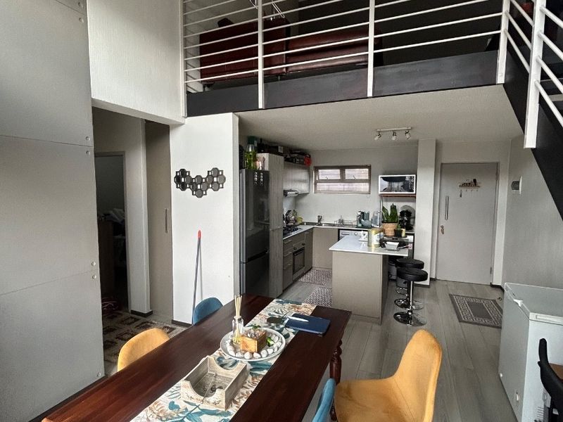 Open-plan apartment living area featuring a modern kitchen with island, laminate flooring, and a mezzanine level with metal railing.
