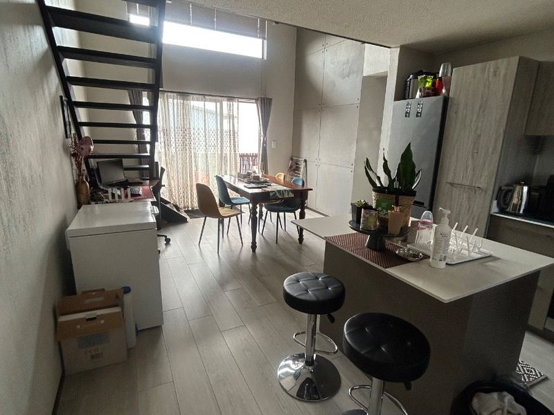 Open-plan living and kitchen area featuring a modern staircase, kitchen island with breakfast bar, and light-toned laminate flooring throughout.