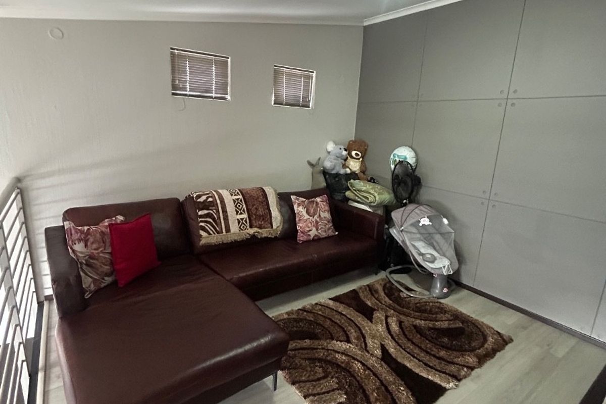 A living room area featuring light-toned laminate flooring, track lighting, and a feature wall with panel detailing.