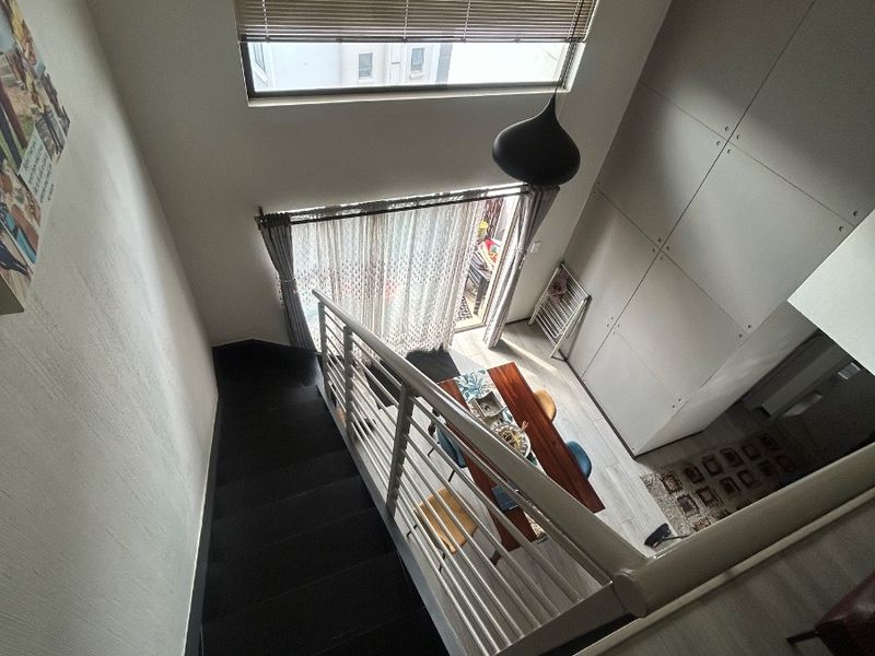A high-angle view of an open-plan living area featuring a modern staircase, double-height ceilings, and large windows providing ample natural light.