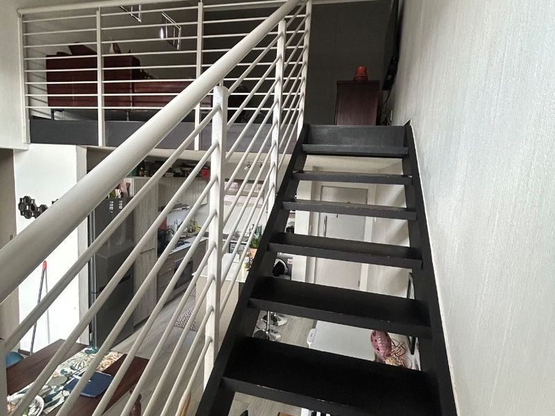 An open-plan apartment interior featuring a modern staircase leading to a mezzanine level, with views overlooking the lower living and kitchen area.