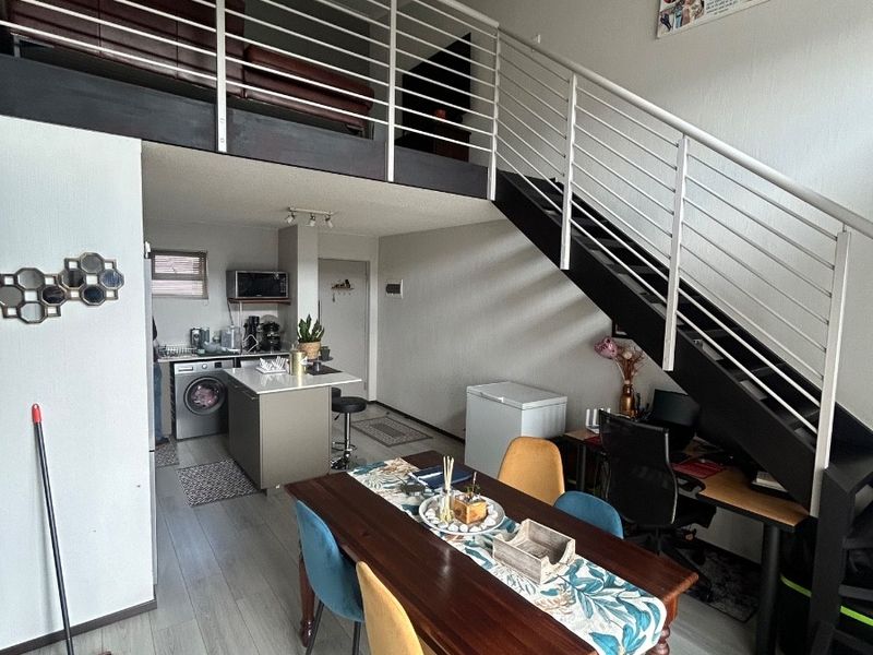Open-plan living area featuring a mezzanine level with a metal staircase, modern laminate flooring, and a functional kitchen island.