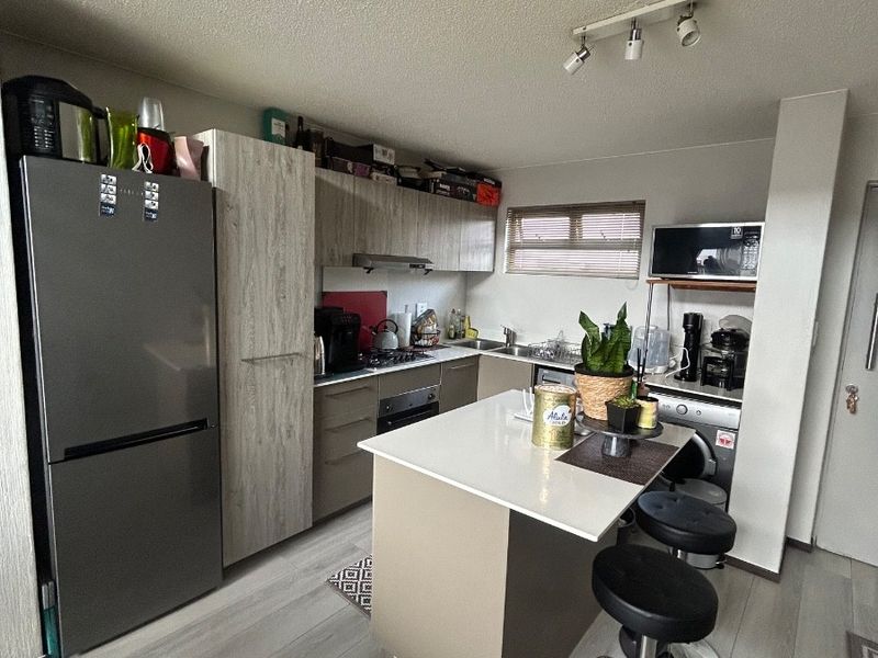 Modern kitchen featuring light wood-tone cabinetry, a central island with stone countertop, built-in oven, hob, and integrated storage solutions.