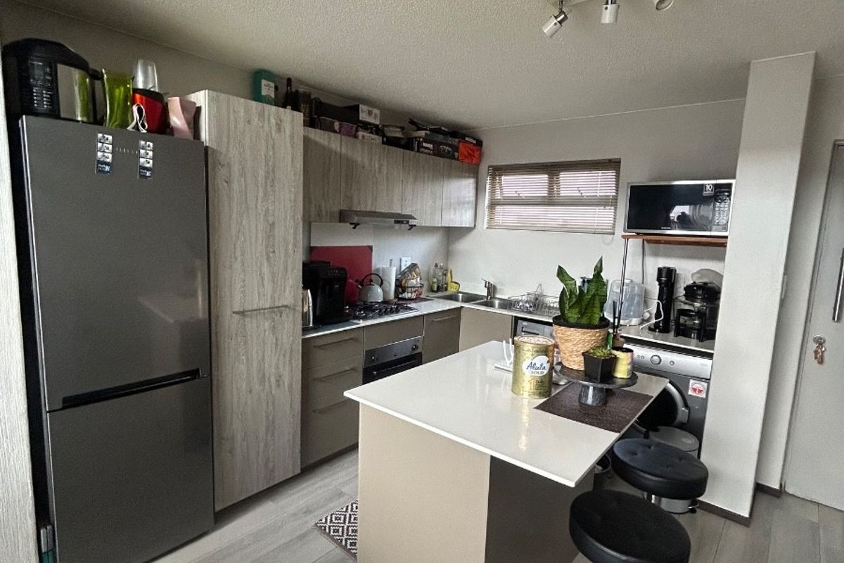 Modern kitchen featuring light wood-tone cabinetry, a central island with stone countertop, built-in oven, hob, and integrated storage solutions.