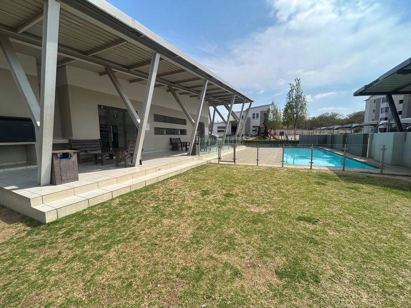 Outdoor communal area featuring a swimming pool with glass fencing and a spacious covered patio with a built-in braai.