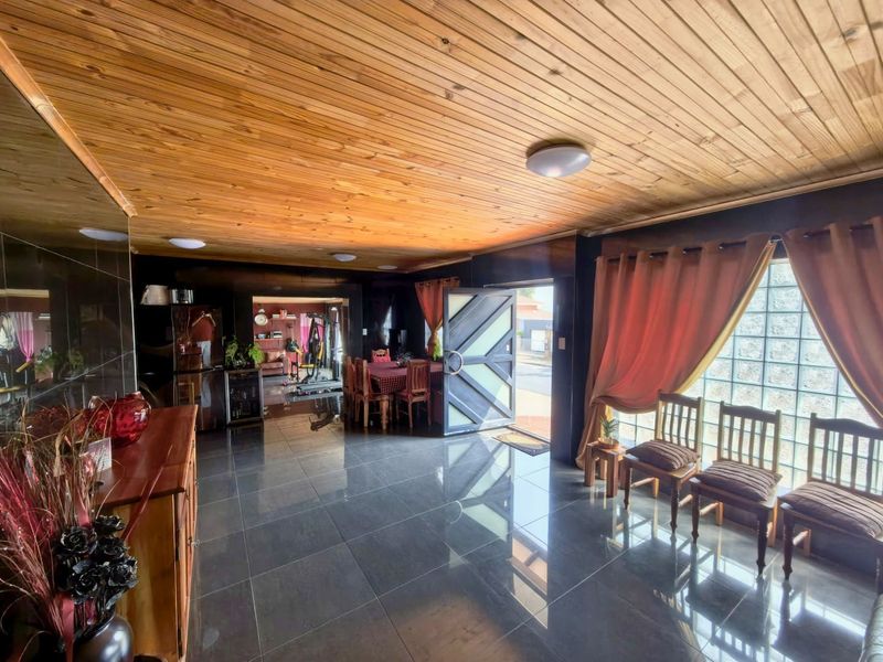 Spacious living area featuring a warm timber tongue and groove ceiling, polished tiled flooring, and a unique glass block feature wall.