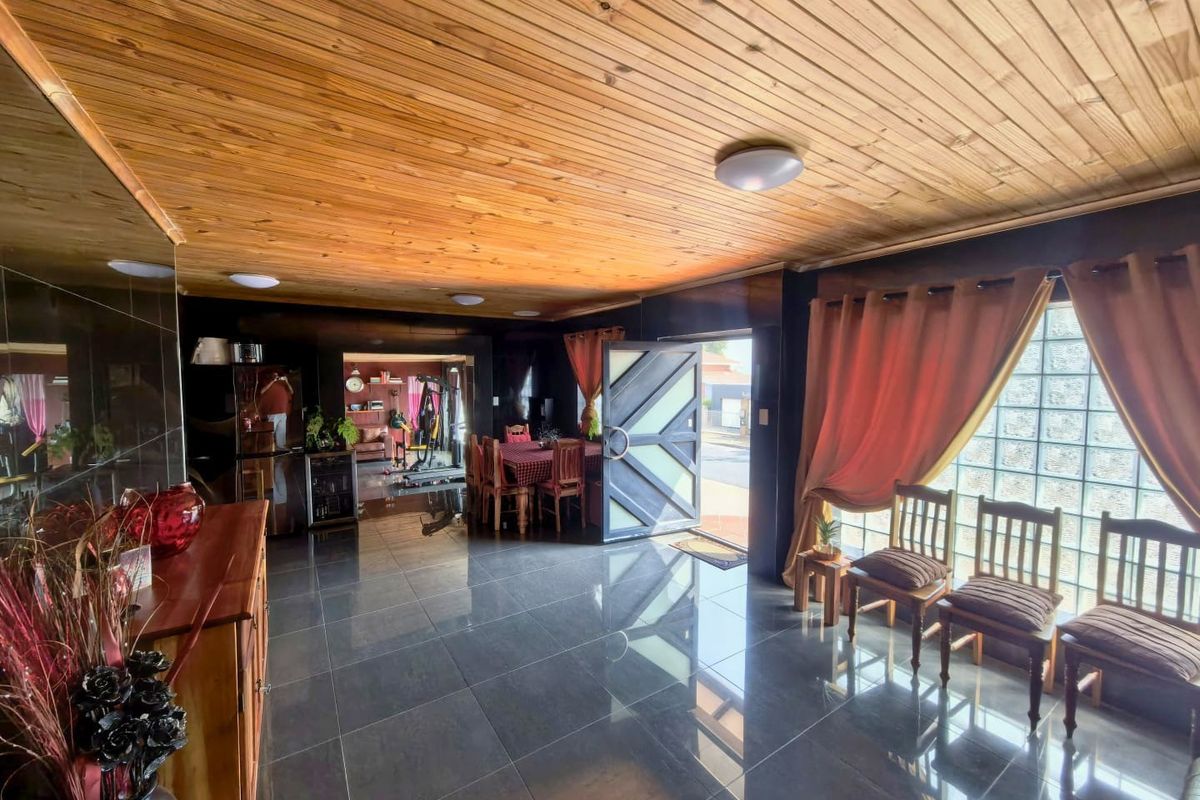Spacious living area featuring a warm timber tongue and groove ceiling, polished tiled flooring, and a unique glass block feature wall.
