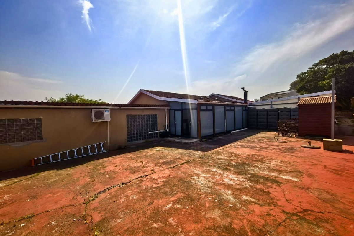 Rear exterior view featuring a large paved patio area, enclosed patio structure, and exterior wall with glass block windows and air conditioning unit.